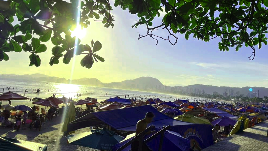 Vista da Praia da Enseada com o por do sol e dos guarda-s&oacute;is. O sol se pondo brilhante no horizonte.