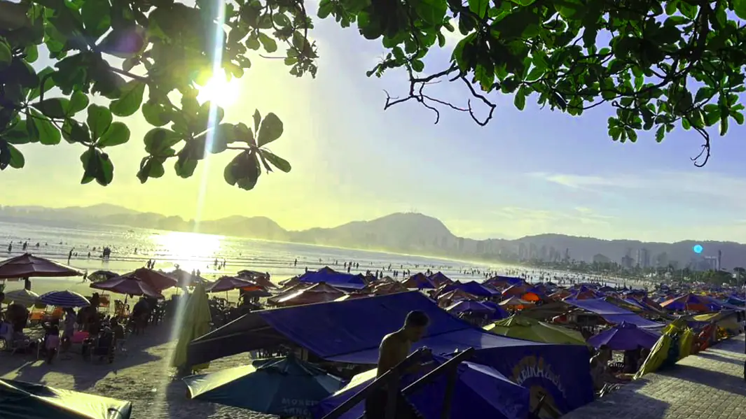 Vista da Praia da Enseada com o por do sol e dos guarda-s&oacute;is. O sol se pondo brilhante no horizonte.