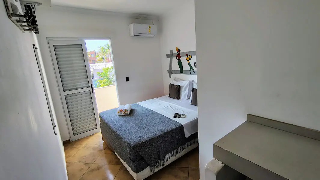 Vista do quarto superior com varanda, com a cama, a tv e o ar condicionado.